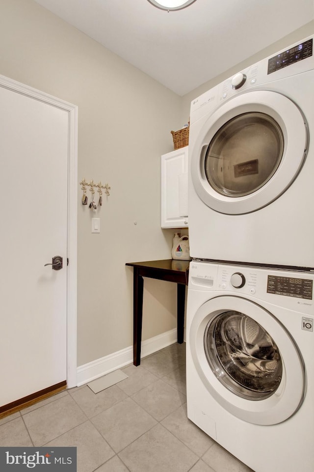 laundry room featuring cabinet space, baseboards, light tile patterned flooring, and stacked washer and clothes dryer