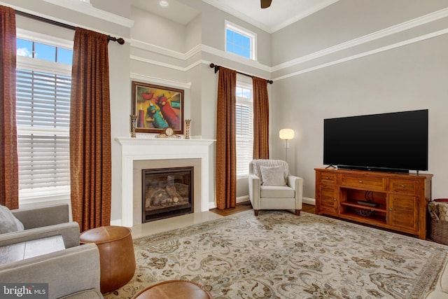 living area featuring baseboards, a fireplace with flush hearth, a ceiling fan, and crown molding