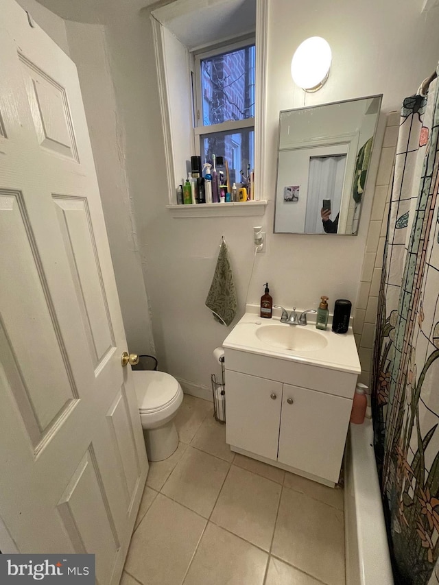 bathroom featuring tile patterned floors, toilet, shower / tub combo with curtain, baseboards, and vanity