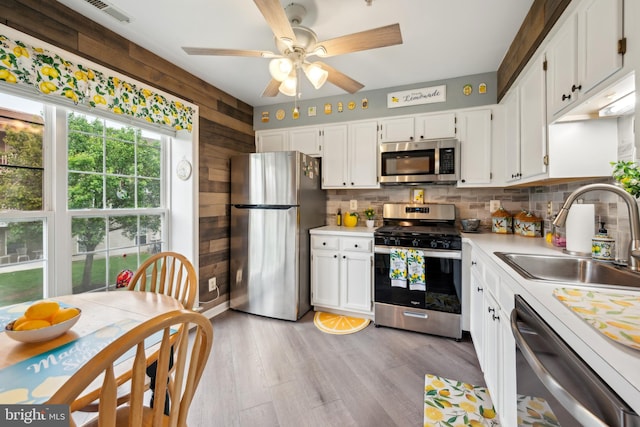 kitchen featuring stainless steel appliances, a sink, light countertops, white cabinets, and wood walls