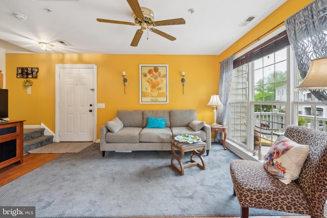 living area with ceiling fan, carpet, and stairway