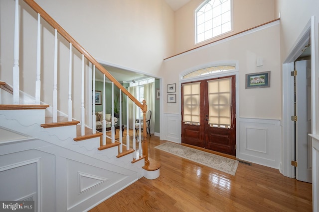 entrance foyer with wood finished floors, visible vents, a towering ceiling, stairway, and wainscoting