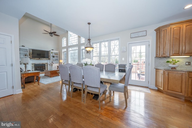 dining space featuring light wood finished floors, a fireplace, a towering ceiling, and a ceiling fan