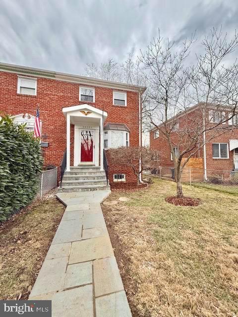 townhome / multi-family property featuring a front lawn, fence, and brick siding