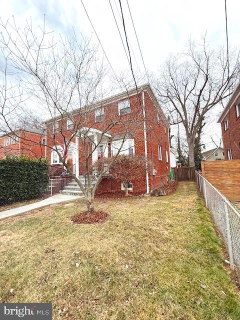 view of front of home featuring brick siding, a front lawn, and fence