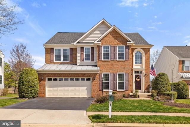 view of front facade with driveway, a standing seam roof, an attached garage, a front lawn, and brick siding