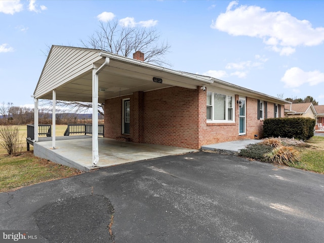 view of property exterior featuring driveway, a chimney, a carport, and brick siding