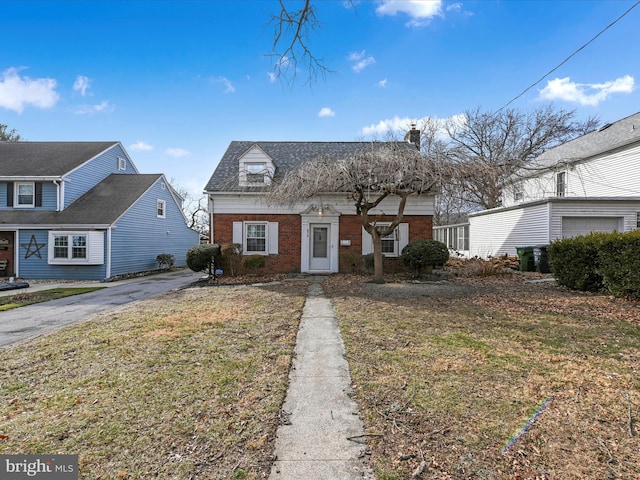 view of front of property with a shingled roof, a front yard, a chimney, and brick siding