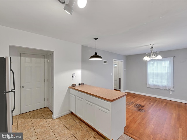 kitchen featuring light countertops, visible vents, freestanding refrigerator, white cabinets, and a peninsula