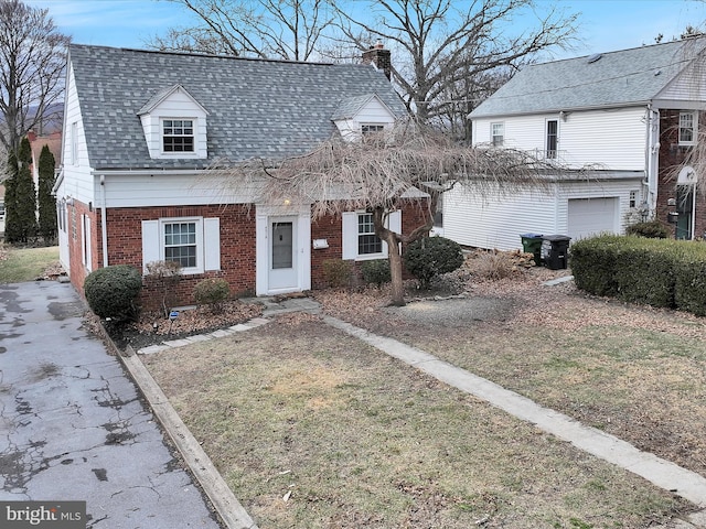 view of front facade with brick siding, roof with shingles, and a chimney