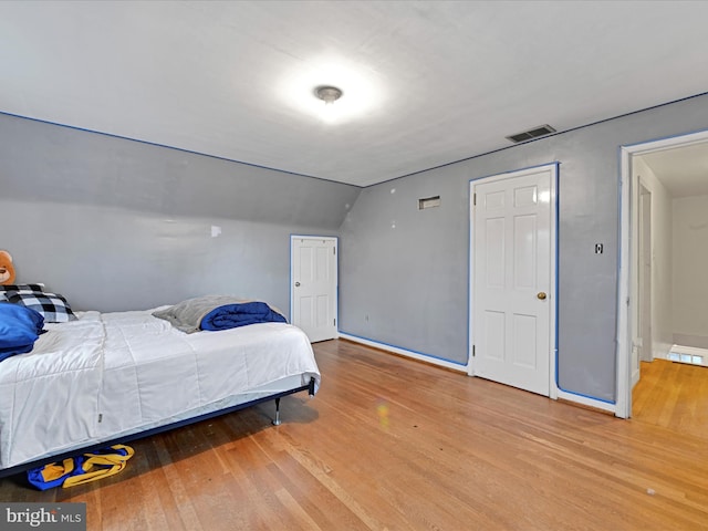 bedroom featuring vaulted ceiling, wood finished floors, visible vents, and baseboards