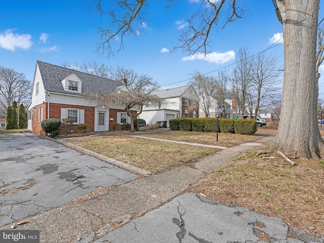 view of front of house featuring a shingled roof, a front yard, brick siding, and a residential view