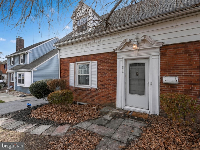 property entrance featuring brick siding and a shingled roof