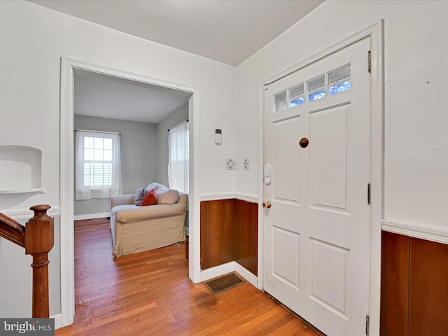 entrance foyer with wooden walls, visible vents, wood finished floors, and wainscoting