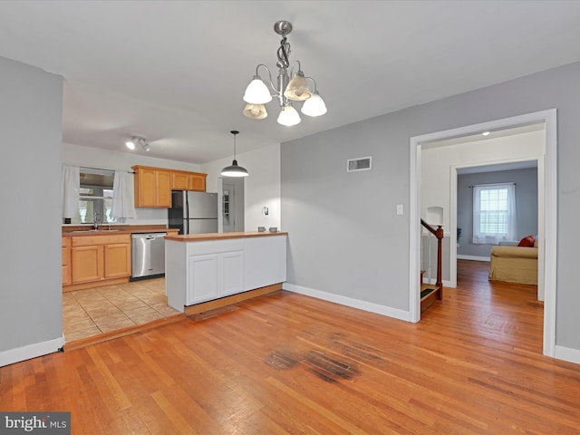 kitchen with stainless steel appliances, a peninsula, a sink, visible vents, and light wood-style floors