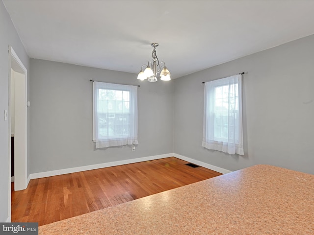 interior space featuring an inviting chandelier, baseboards, visible vents, and wood finished floors