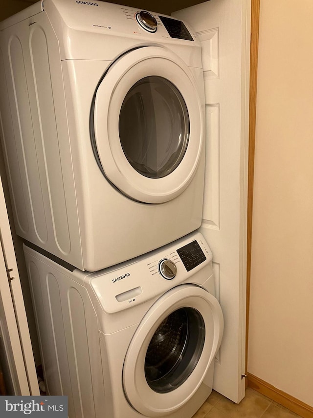 clothes washing area featuring baseboards, stacked washer and clothes dryer, light tile patterned flooring, and laundry area