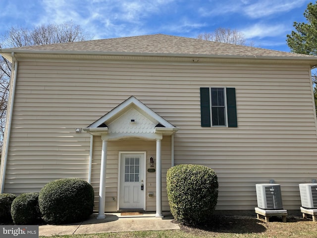 view of exterior entry with cooling unit and a shingled roof