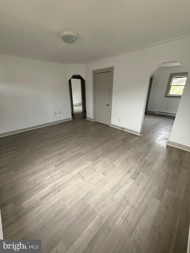 interior space featuring arched walkways, a baseboard radiator, baseboards, and wood finished floors