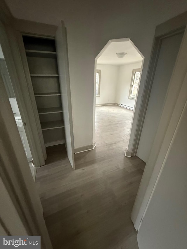 hallway with arched walkways, a baseboard radiator, wood finished floors, and baseboards