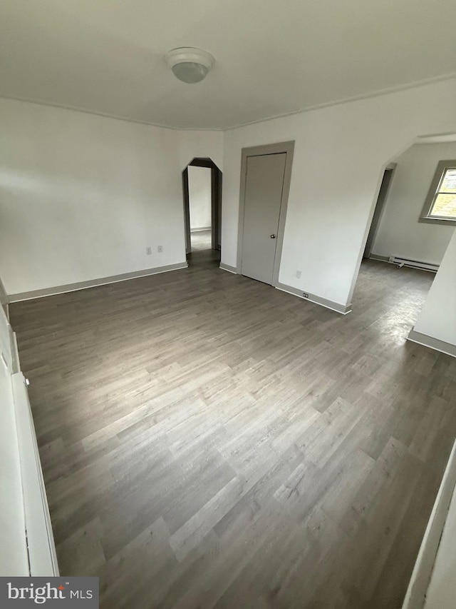 unfurnished bedroom with arched walkways, baseboard heating, wood finished floors, and baseboards