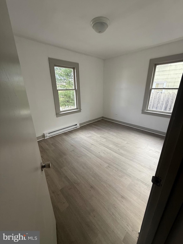 unfurnished room with a baseboard heating unit, wood finished floors, and baseboards