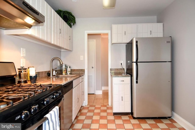 kitchen with under cabinet range hood, a sink, white cabinetry, appliances with stainless steel finishes, and light stone countertops