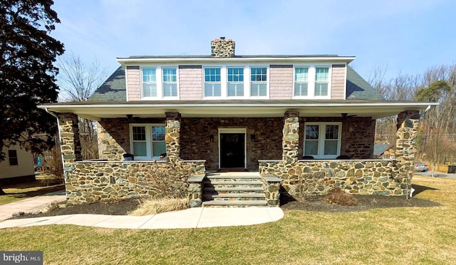 view of front of property featuring a front yard, covered porch, stone siding, and a chimney