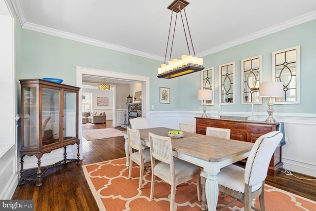 dining area with a decorative wall, a wainscoted wall, dark wood-type flooring, and ornamental molding