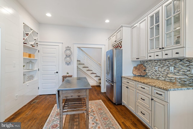 kitchen with decorative backsplash, glass insert cabinets, dark wood-style floors, and freestanding refrigerator