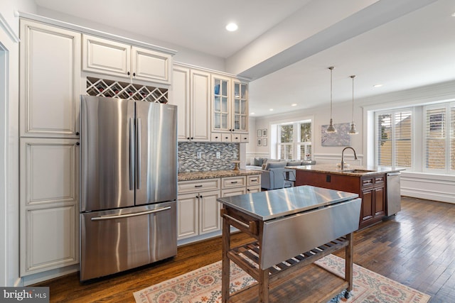 kitchen featuring backsplash, glass insert cabinets, dark wood-type flooring, stainless steel appliances, and a kitchen island with sink