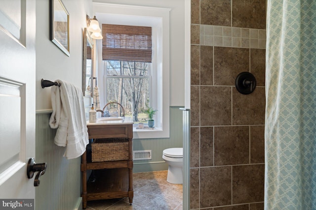 bathroom featuring visible vents, toilet, vanity, and a tile shower