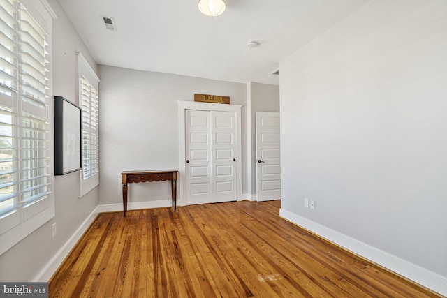 unfurnished bedroom featuring visible vents, wood finished floors, baseboards, and a closet