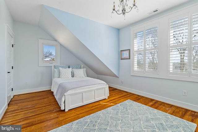 bedroom featuring visible vents, a notable chandelier, wood finished floors, baseboards, and vaulted ceiling