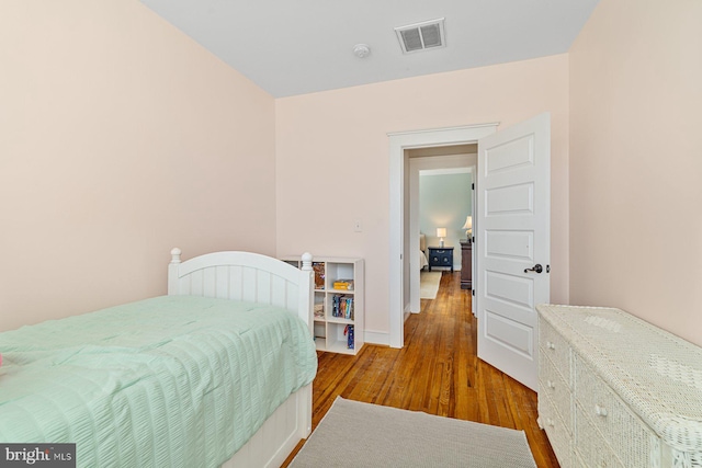 bedroom with wood finished floors, visible vents, and baseboards