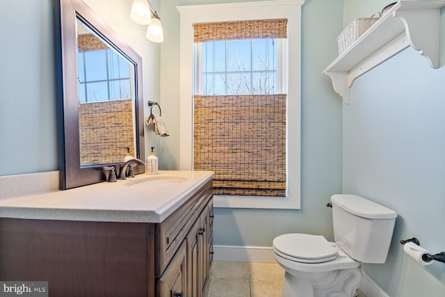 half bathroom with baseboards, toilet, a healthy amount of sunlight, and vanity