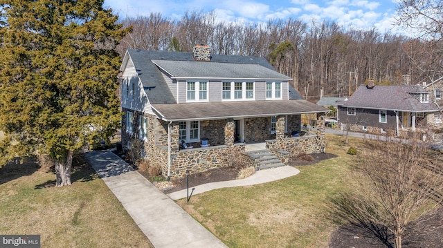 view of front of home featuring a porch, a chimney, a front lawn, concrete driveway, and stone siding