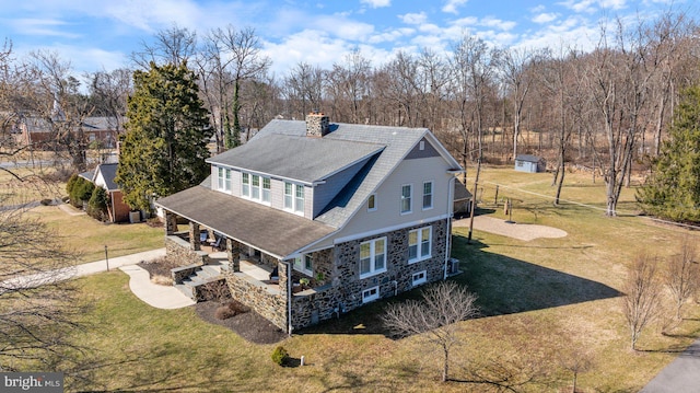 back of property featuring a yard, a patio area, stone siding, and a chimney