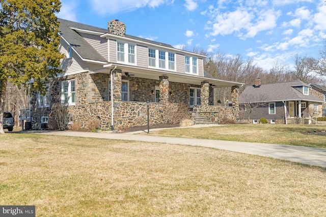 view of front of property featuring a front lawn, covered porch, stone siding, and a chimney