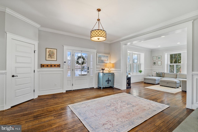 foyer entrance featuring dark wood-style floors, a decorative wall, wainscoting, and ornamental molding