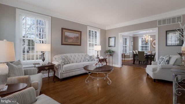 living area with visible vents, baseboards, wood finished floors, crown molding, and a notable chandelier