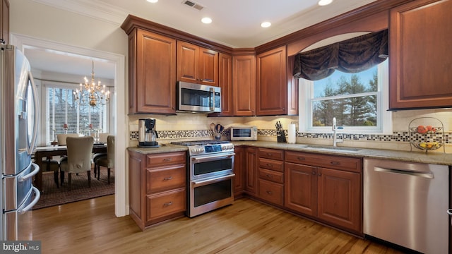 kitchen with appliances with stainless steel finishes, light wood-type flooring, a sink, and visible vents