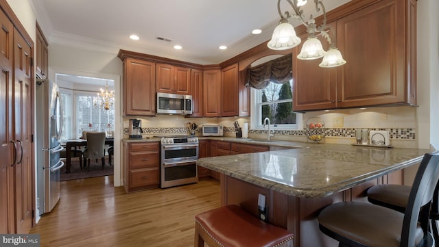 kitchen with appliances with stainless steel finishes, brown cabinets, a breakfast bar, light stone counters, and a peninsula