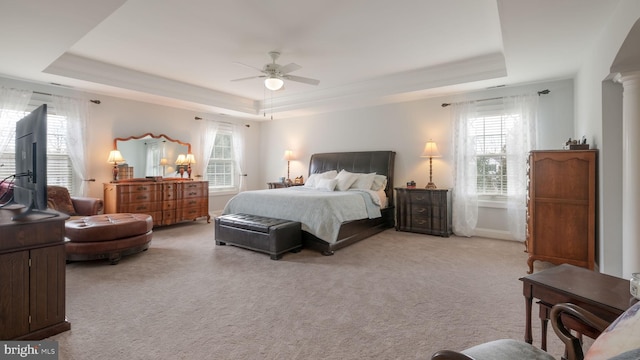 bedroom with light carpet, ceiling fan, decorative columns, and a raised ceiling