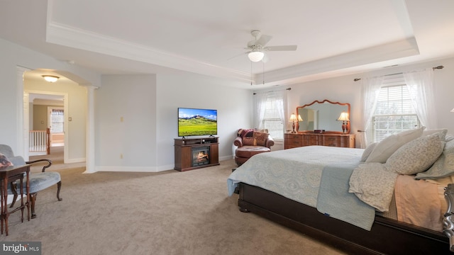 bedroom with light carpet, decorative columns, arched walkways, baseboards, and a tray ceiling