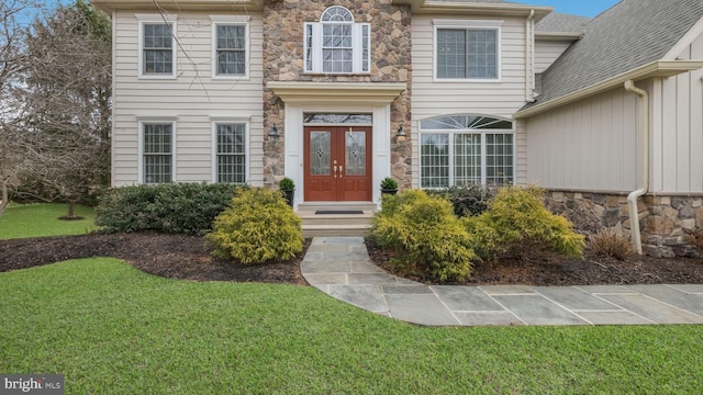 entrance to property featuring stone siding, french doors, and a yard