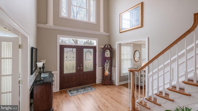 entryway featuring light wood-type flooring, a healthy amount of sunlight, stairway, and a towering ceiling