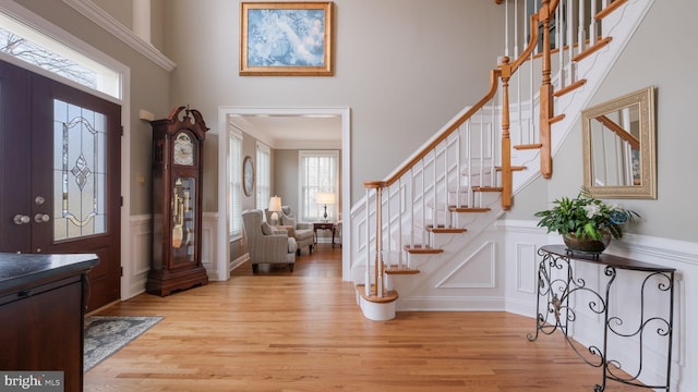 entryway featuring light wood finished floors, a towering ceiling, a wainscoted wall, stairway, and a decorative wall