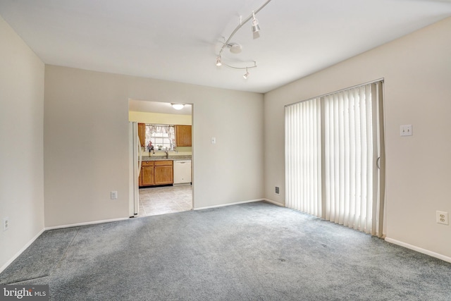 unfurnished room featuring track lighting, baseboards, and light carpet