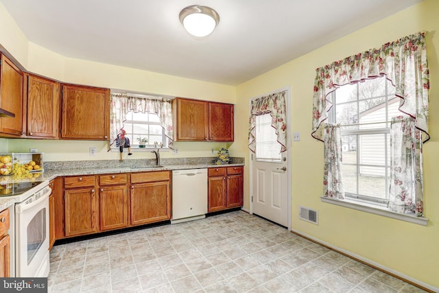 kitchen with brown cabinetry, visible vents, white appliances, and a sink